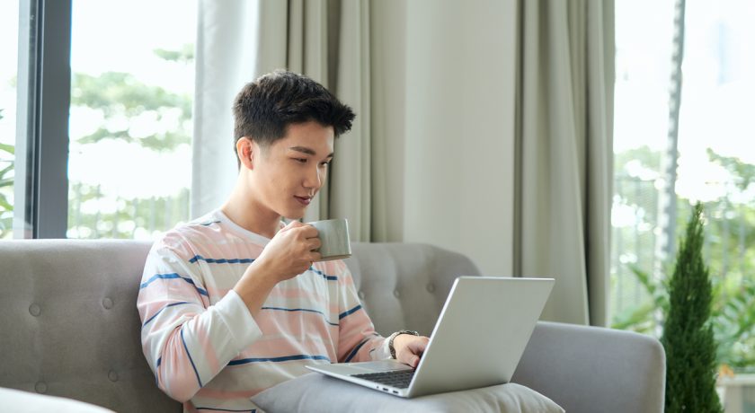 Man works for laptop. He rejoices in the search result, holding a cup of coffee